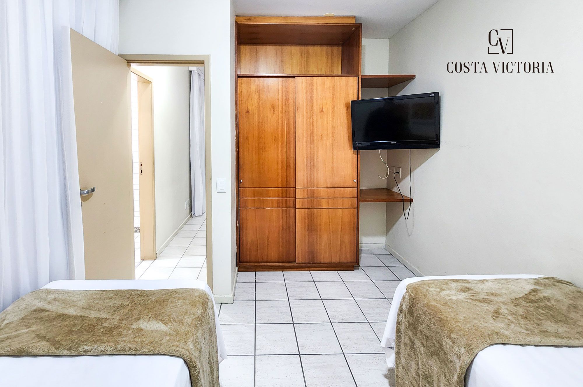 Un dormitorio con dos camas, un armario de madera, un televisor y un letrero que dice "COSTA VICTORIA".