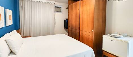 Quarto de hotel com cama grande, armário de madeira e cozinha compacta.