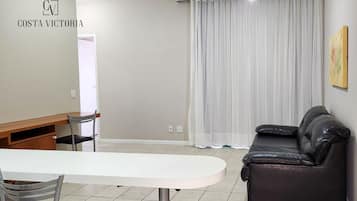 Sala de estar com uma mesa branca, sofá de couro preto e área de jantar com cadeiras.