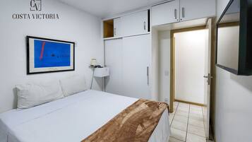 Habitación de hotel con cama, escritorio, silla, televisor y puerta.