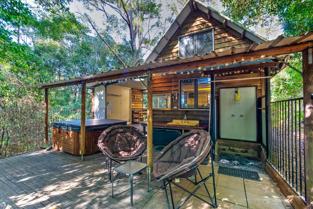 A wooden cabin with a covered patio, two hot tubs, and a small bar area.