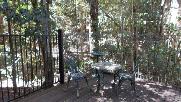 A wooden deck with a metal table and chairs, surrounded by a metal fence and trees.