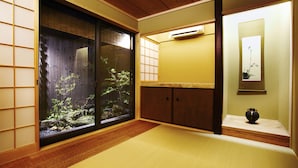A traditional Japanese room with tatami flooring, a sliding door with a view of a garden, a small cabinet, and a wall-mounted air conditioner. - Kyoto Tradition With Modern Luxury, Family Friendly in Excellent Location (Kyoto)