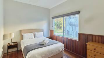 Camera da letto con un letto, un comodino, una cassettiera e una finestra vista alberi.