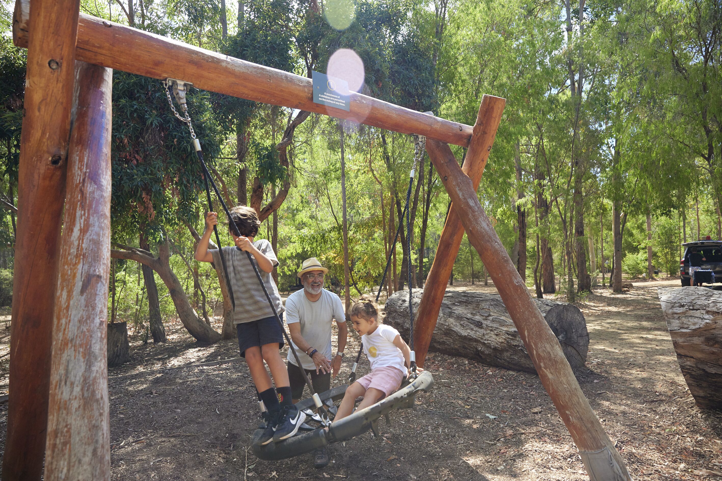A wooden swing set in a wooded area with people using it.