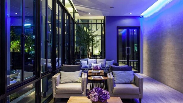 A modern interior with a sofa set, a coffee table, and a large window providing a view of the outside. - Hug Nimman Hotel (Chiang Mai)