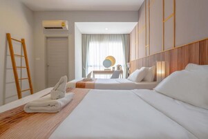 Habitación de hotel con dos camas, un escritorio y una silla. Se observa una unidad de aire acondicionado en la pared y una escalera de madera apoyada contra la pared.