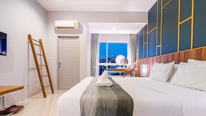 A hotel room with a large bed, a desk, a chair, and a view of a cityscape. - Hug Nimman Hotel (Chiang Mai)