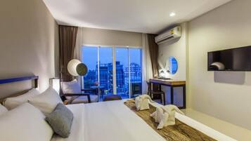 Habitación de hotel con una cama grande, un escritorio, una silla y vistas a la ciudad a través de la ventana.