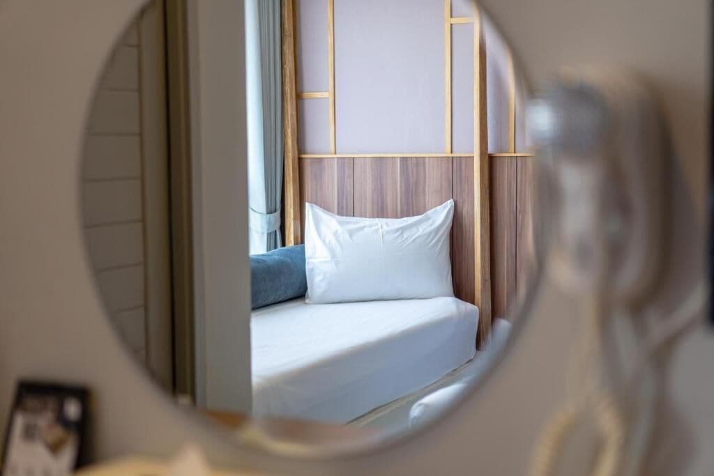 A bed with white bedding and a blue pillow, framed by a wooden headboard and a wall with a grid pattern.