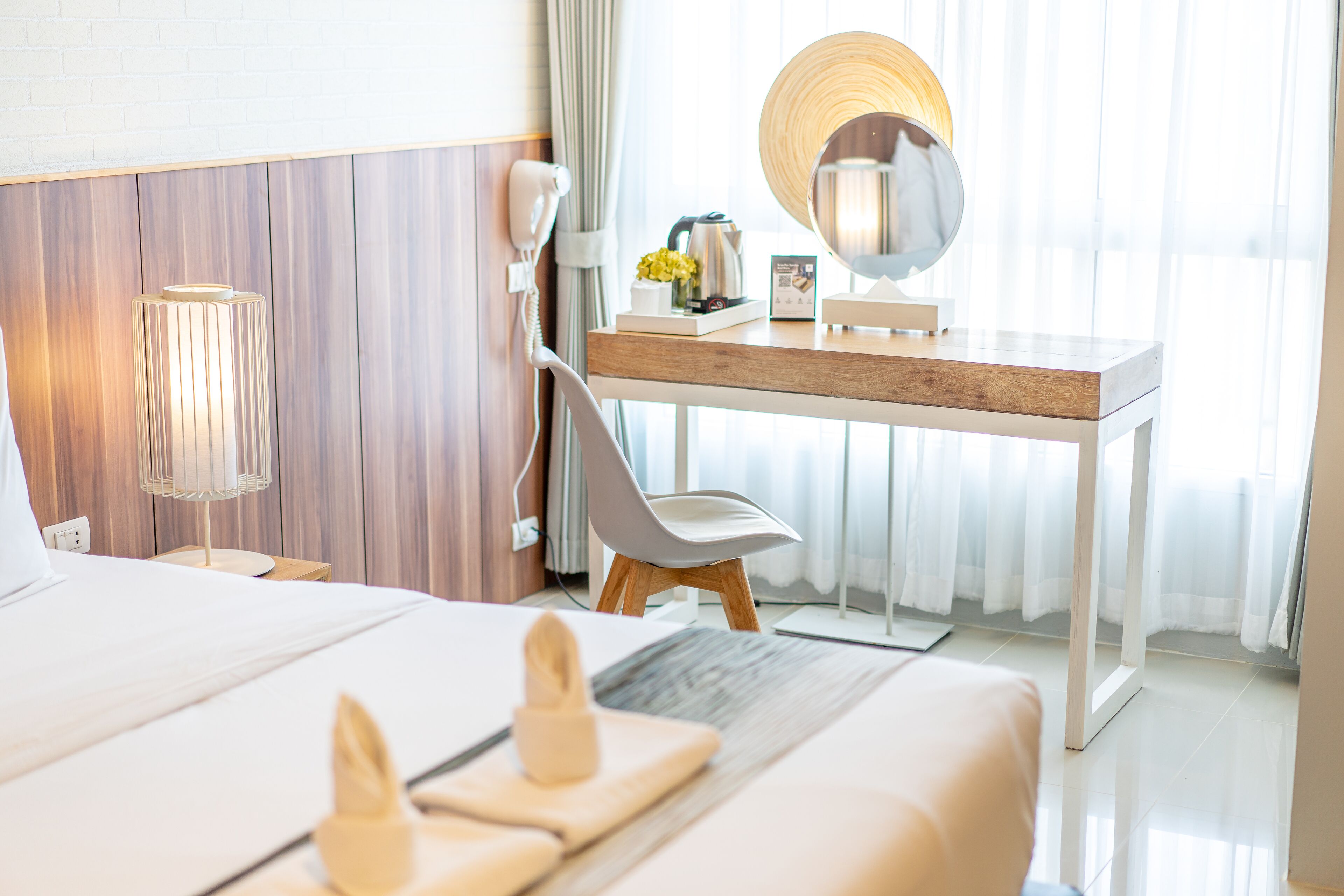 Habitación de hotel con cama, escritorio con espejo, silla, lámpara y ventana con cortinas.