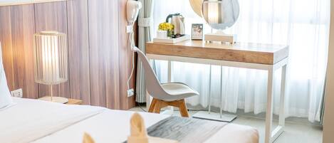 Habitación de hotel con cama, escritorio con espejo, silla, lámpara y ventana con cortinas.
