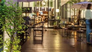 An outdoor patio area with tables and chairs, a glass wall, and a building in the background. - Hug Nimman Hotel (Chiang Mai)