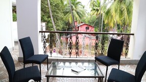 A balcony with a glass table and four black chairs, overlooking a red building and palm trees. - Bay luxe (Anjuna)
