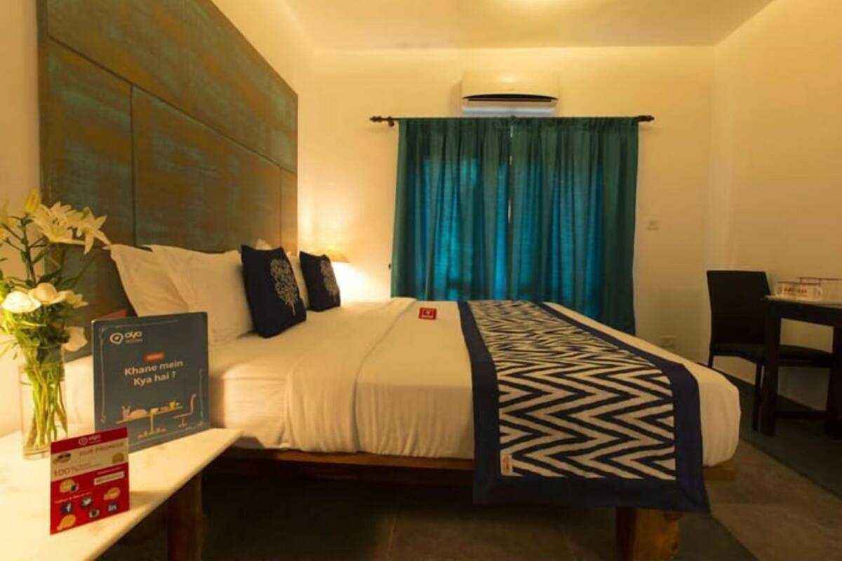 A hotel room with a bed, a desk, and a chair. There is a vase with flowers on the desk and a sign on the wall.