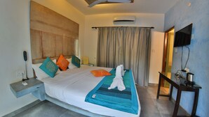 A hotel room with a bed, a nightstand, a desk, a television, and a ceiling fan. - Bay luxe (Anjuna)