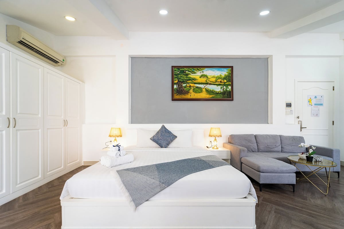 Een hotelkamer met een groot bed, een grijze bank, een klein tafeltje en een schilderij aan de muur.
