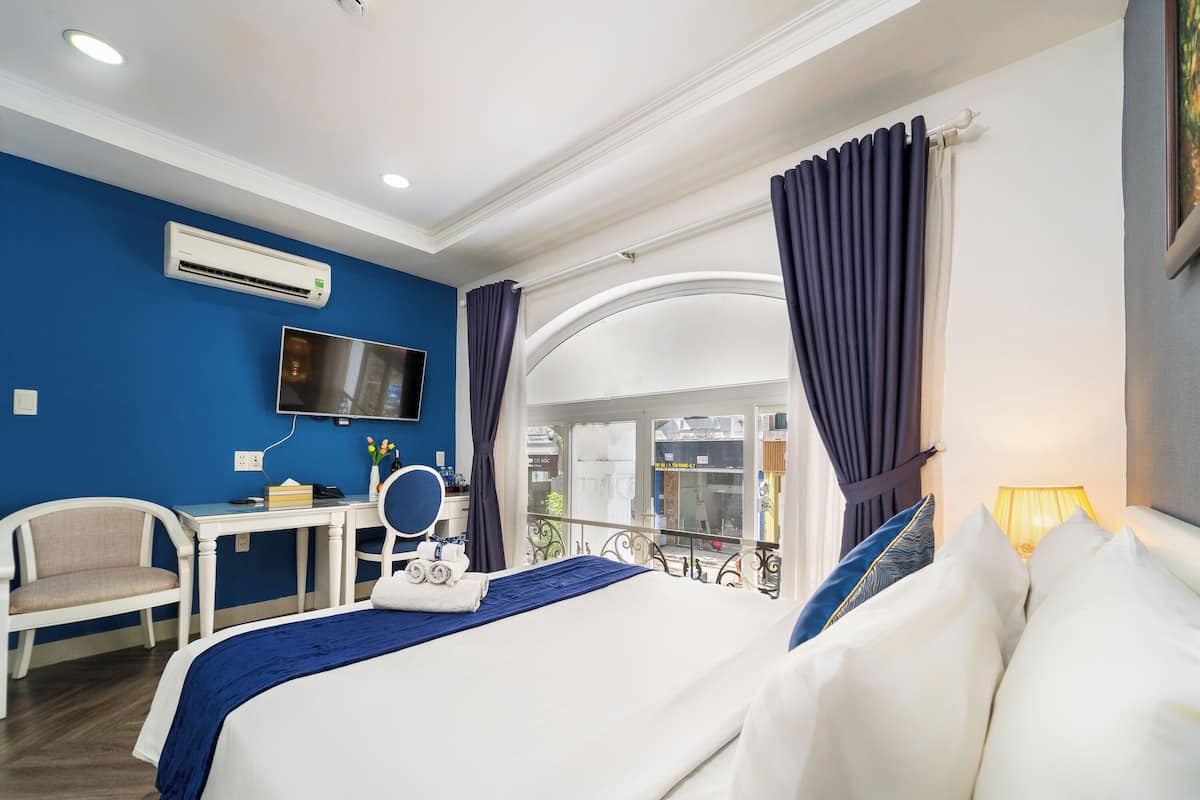Een hotelkamer met een bed, een bureau met stoel, een televisie en een balkon met gordijnen.