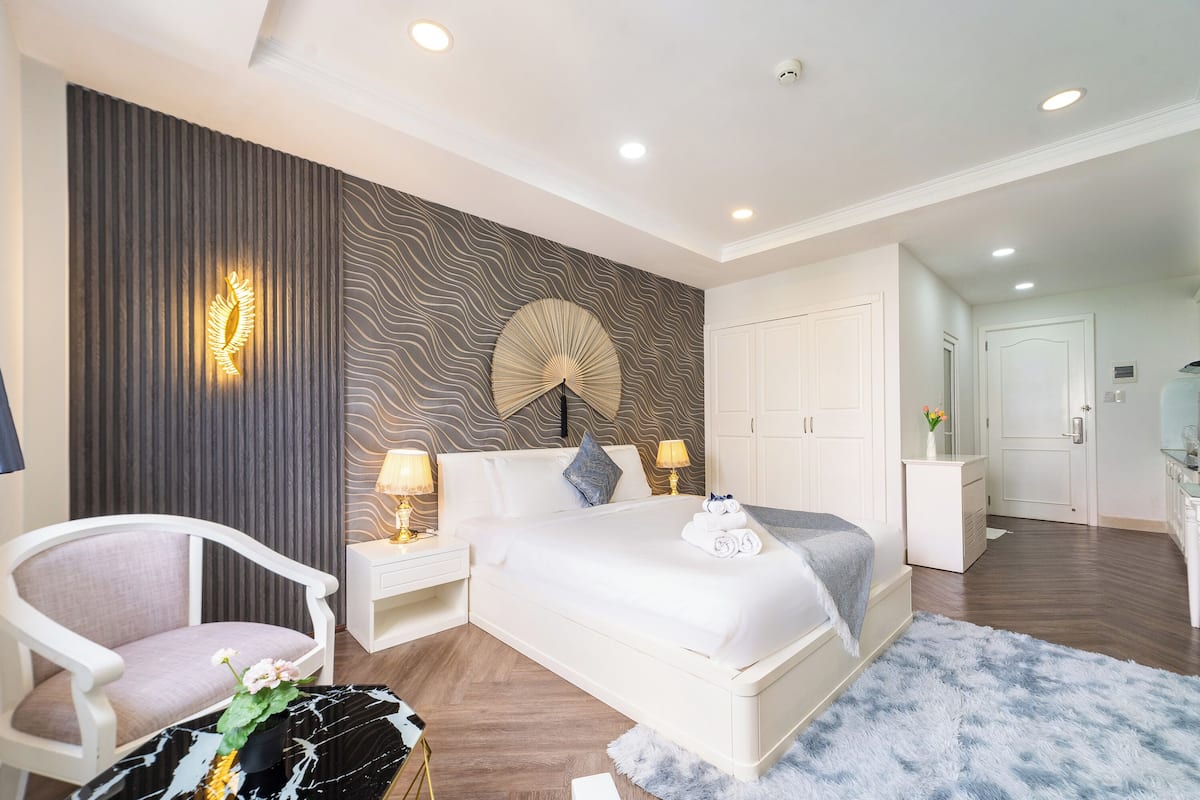 Een moderne hotelkamer met een groot bed, een zithoek met een fauteuil, een kaptafel en een badkamer op de achtergrond.