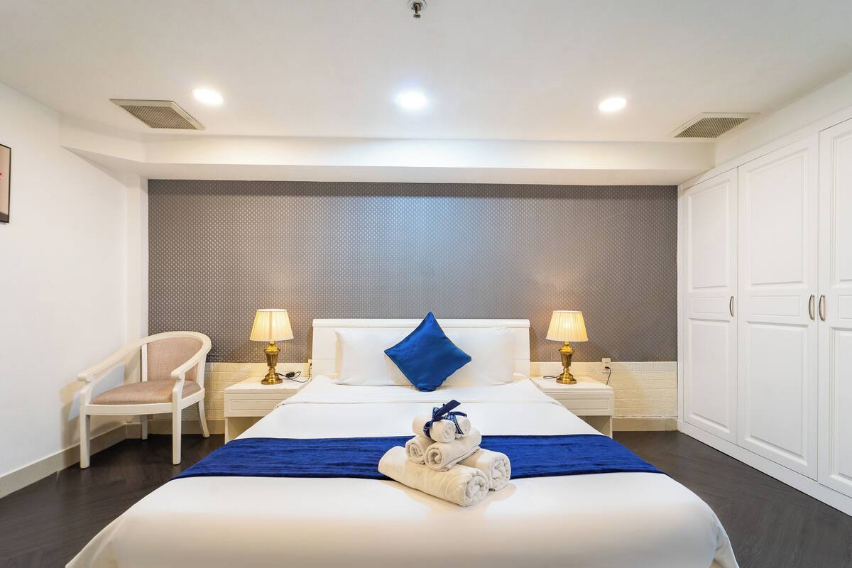 Een hotelkamer met een groot bed, twee nachtkastjes met lampen, een stoel en een garderobe.