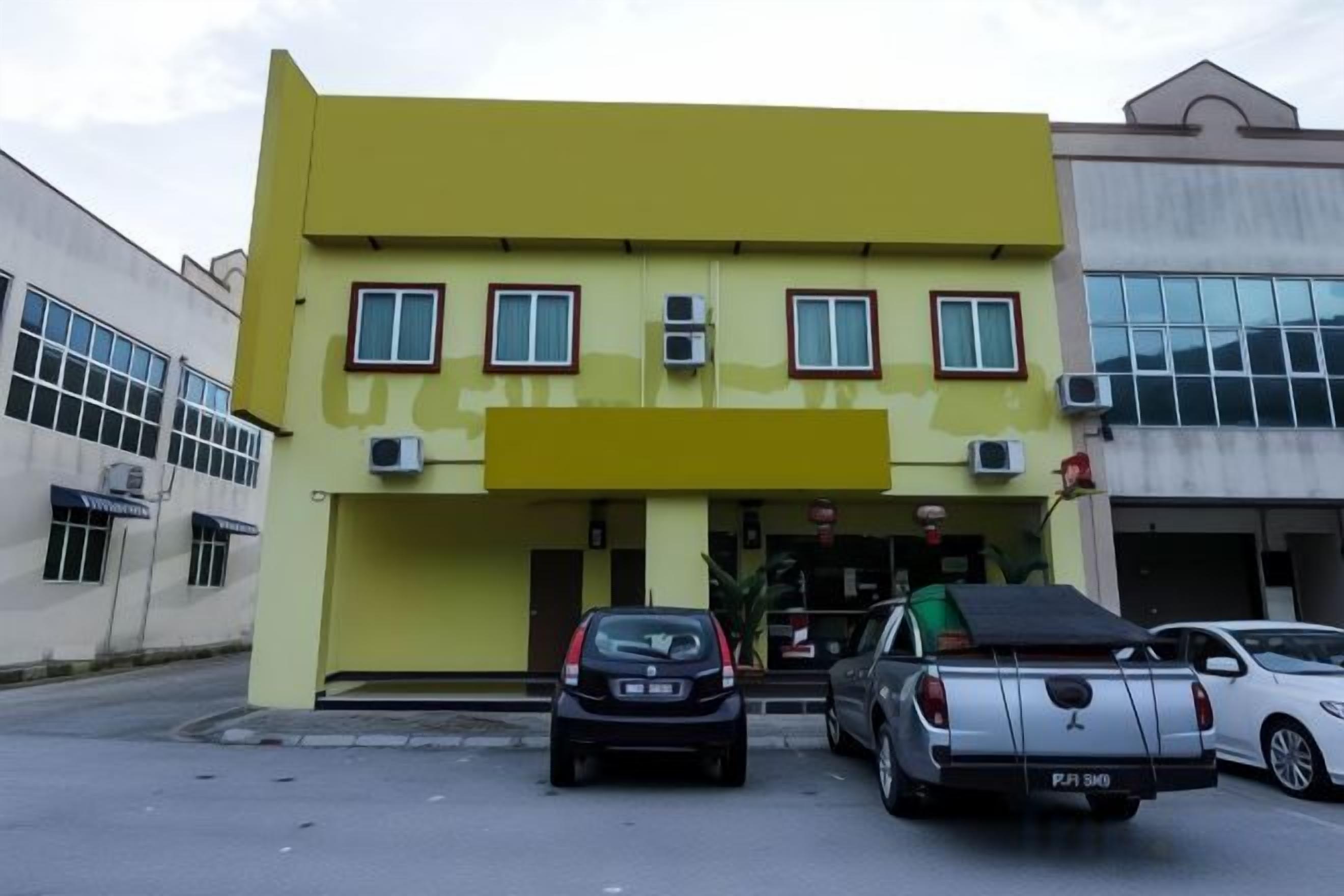 Un bâtiment jaune avec un toit plat, deux fenêtres visibles et une voiture garée devant.