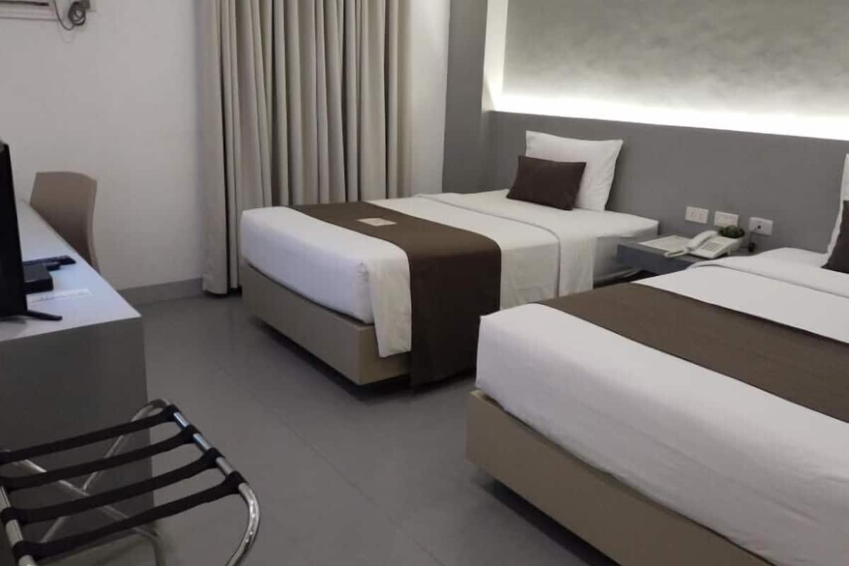 A hotel room with two beds, a desk with a computer, a chair, and a telephone.