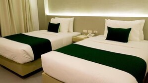 Habitación de hotel con dos camas, cada una con ropa blanca de cama y almohadones verdes, una mesita de noche con un teléfono y una cortina a la izquierda.