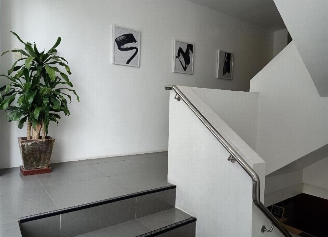 Un escalier avec une rampe métallique, une plante en pot et trois œuvres d’art abstraites accrochées au mur.
