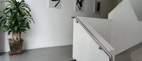 Un escalier avec une rampe métallique, une plante en pot et trois œuvres d’art abstraites accrochées au mur.