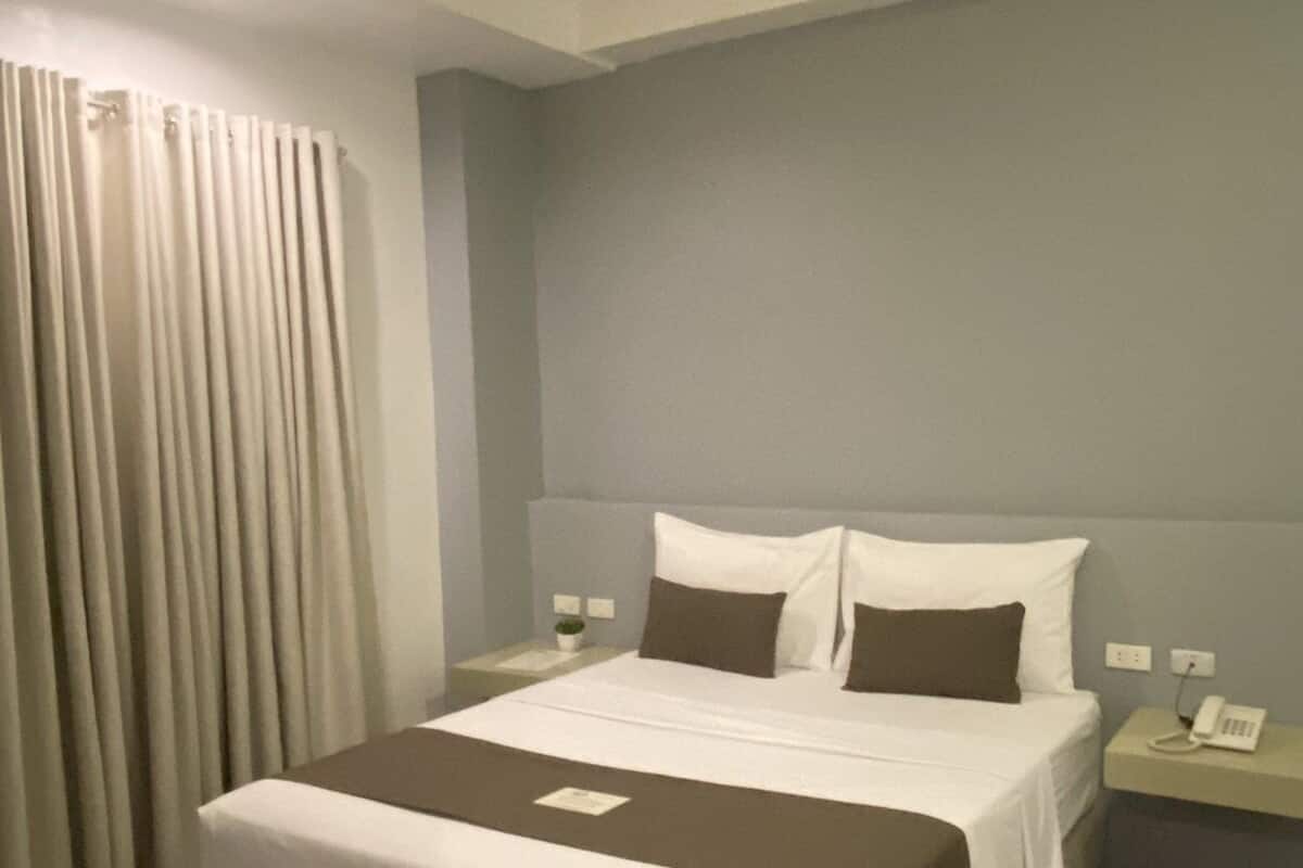 A hotel room with a large bed, a bedside table with a phone, and a window with curtains.