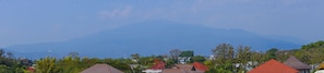 A residential area with houses having red-tiled roofs, surrounded by greenery and mountains in the background.