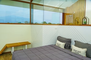A bedroom with a large window, a bed with pillows, and a wooden bench.