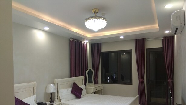 A hotel room with two beds, a bedside table with a lamp, a mirror, a window with curtains, and an air conditioning unit. - Hoang Giang Hotel (Hai Phong)