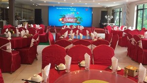A banquet hall with round tables set for a summer event, featuring a large screen displaying a 'Hello Summer' message. - Hoang Giang Hotel (Hai Phong)