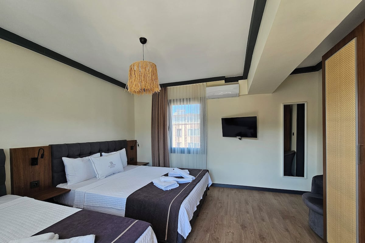 Une chambre d’hôtel avec deux lits, une télévision et une grande fenêtre avec des rideaux.