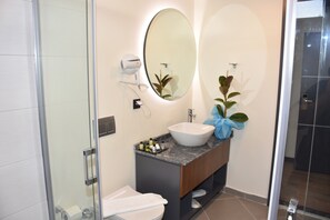A modern bathroom with a glass shower enclosure, a white sink, and a large oval mirror. - Er Turistik Hotel (Dikili)