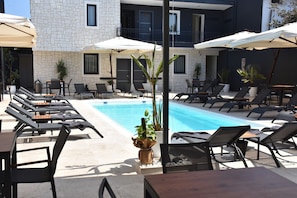 A poolside area with lounge chairs and umbrellas, a stone building with a pool, and potted plants. - Er Turistik Hotel (Dikili)