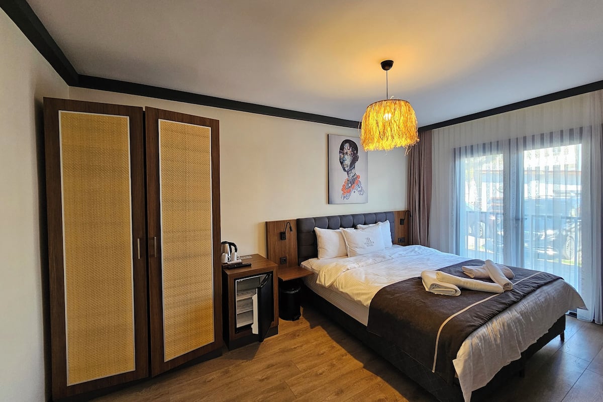 Une chambre d’hôtel avec un lit, une table de chevet, une armoire et une grande fenêtre avec des rideaux.