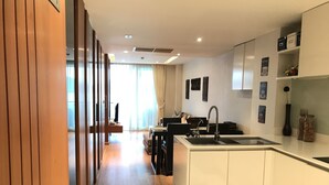 A modern kitchen with a central island, a dining area with a sofa, and a view to a living room. - Privilege Panoramic Sea View (Patong)