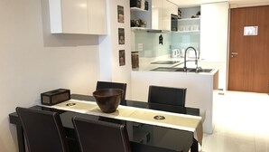A modern kitchen with white cabinets, a glass island, and a dining area with a glass table and chairs. - Privilege Panoramic Sea View (Patong)