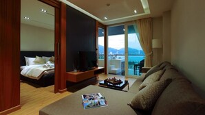 A hotel room with a bed, a TV, a sofa, and a balcony with a view. - Privilege Panoramic Sea View (Patong)