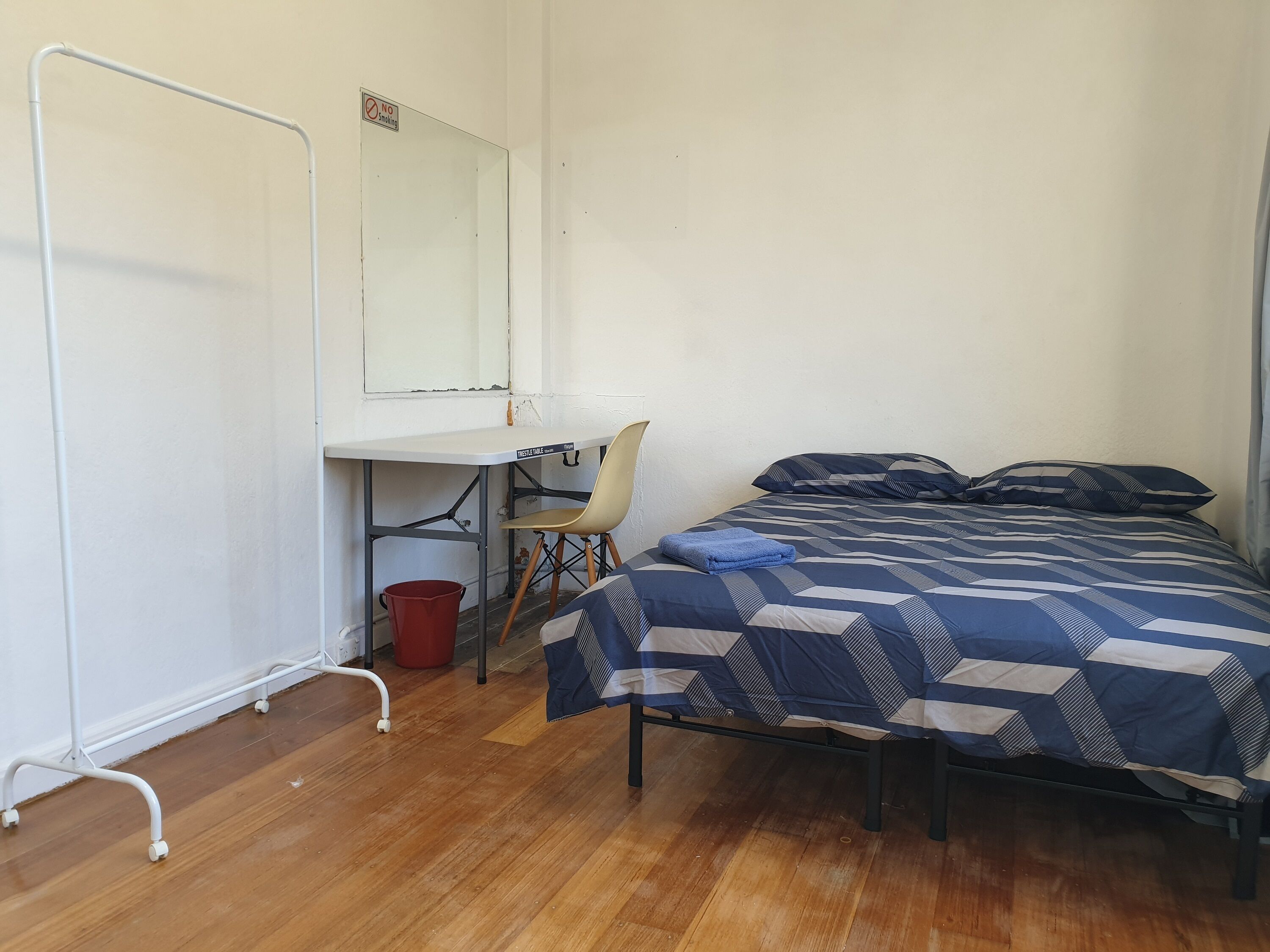 A bedroom with a bed, a desk, a chair, and a red bucket.