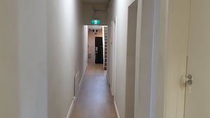 En smal gang med hvide vægge og trægulv, der fører til et rum med en dør og et vindue.