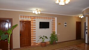 A hallway with wooden doors, a flat-screen TV mounted on the wall, potted plants, and a patterned carpet. - Altamira (Karakol)