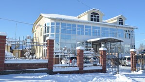 A large building with a glass facade, a covered entrance, and a snow-covered roof. - Altamira (Karakol)
