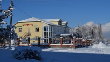 A two-story building with a yellow facade and large windows, surrounded by snow-covered ground and trees.