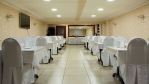 A conference room with rows of tables and chairs, a television mounted on the wall, and a chandelier. - Altamira (Karakol)