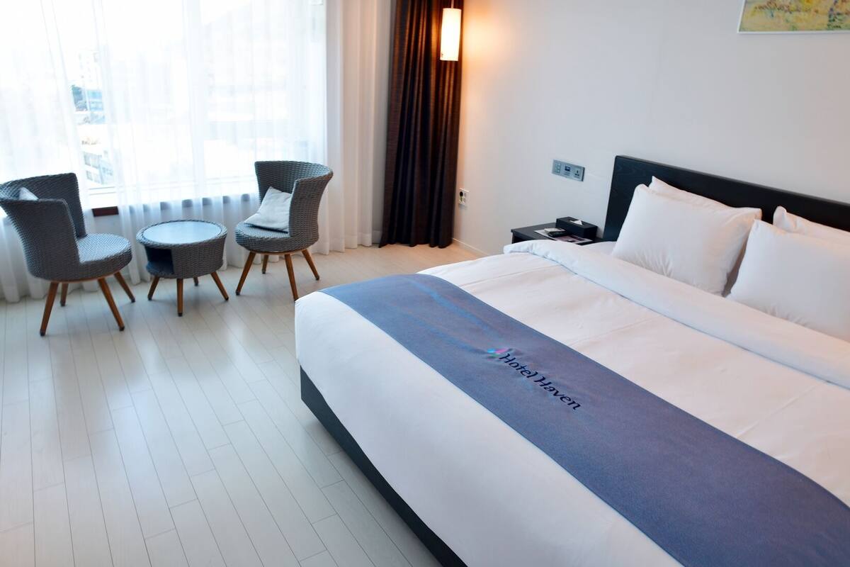 Hotellihuone, jossa on suuri sänky, kaksi tuolia, pieni pöytä ja yöpöytä.