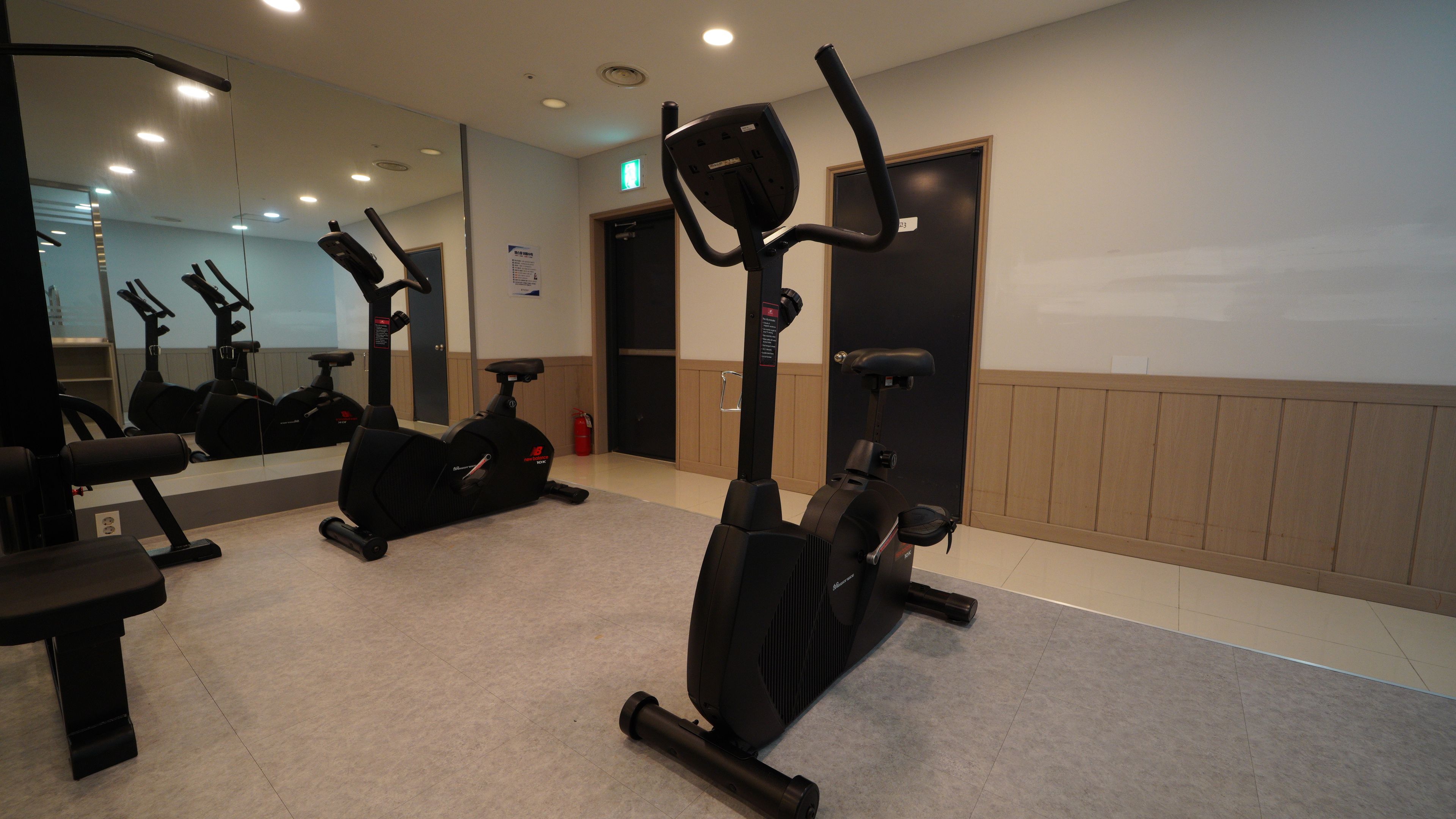 A gym with stationary bikes, a bench, and a mirror reflecting the equipment.