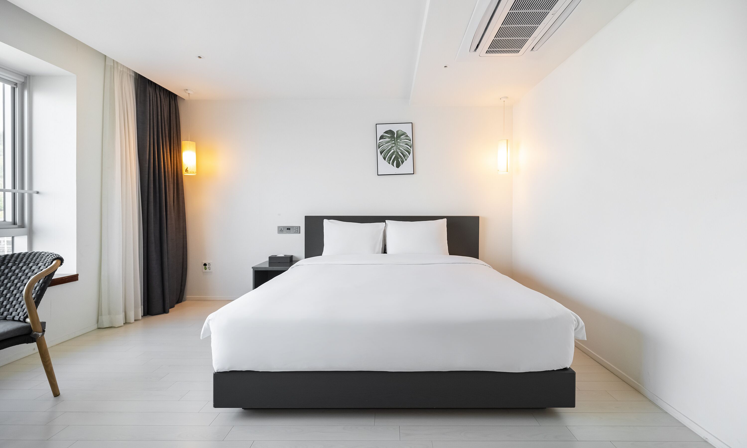 A modern hotel room with a large bed, a chair, a nightstand, and a wall-mounted artwork.